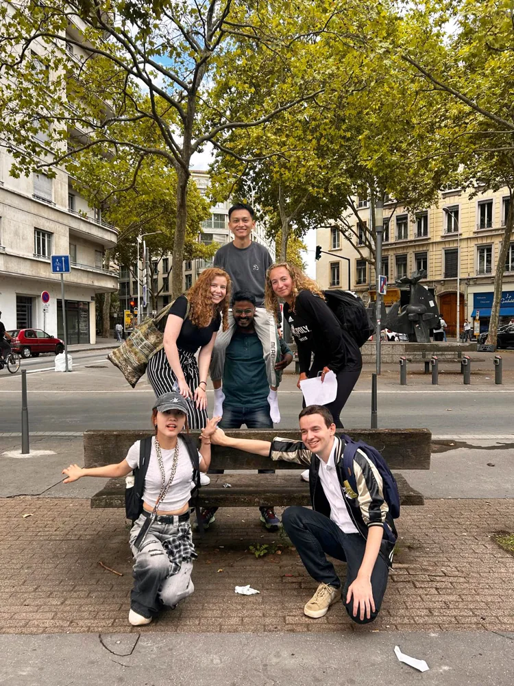 A group of friends posing together by a bench on a tree-lined city street