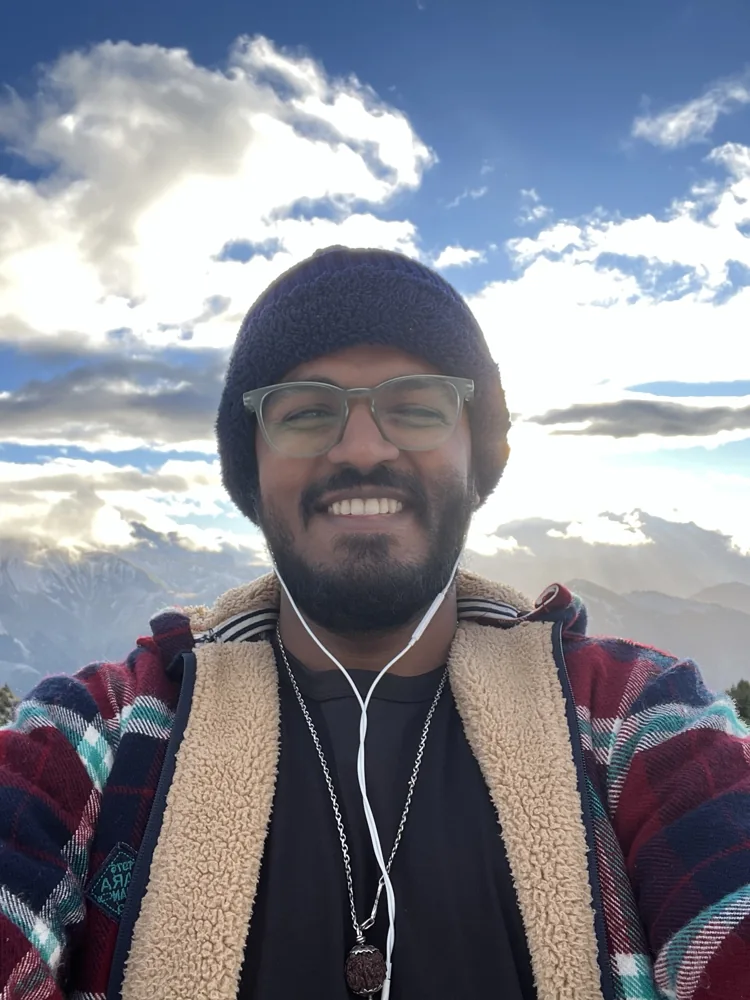 Shivam in a beanie and scarf beneath a cloudy sky