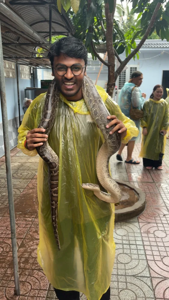 Shivam wearing a yellow rain poncho and holding a large snake across his shoulders